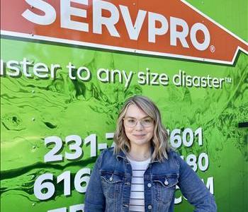 Female employee Katie standing in front of green SERVPRO vehicle