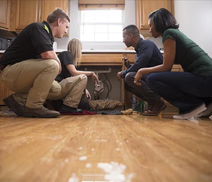 Homeowners and SERVPRO technicians crouched down in water affected kitchen